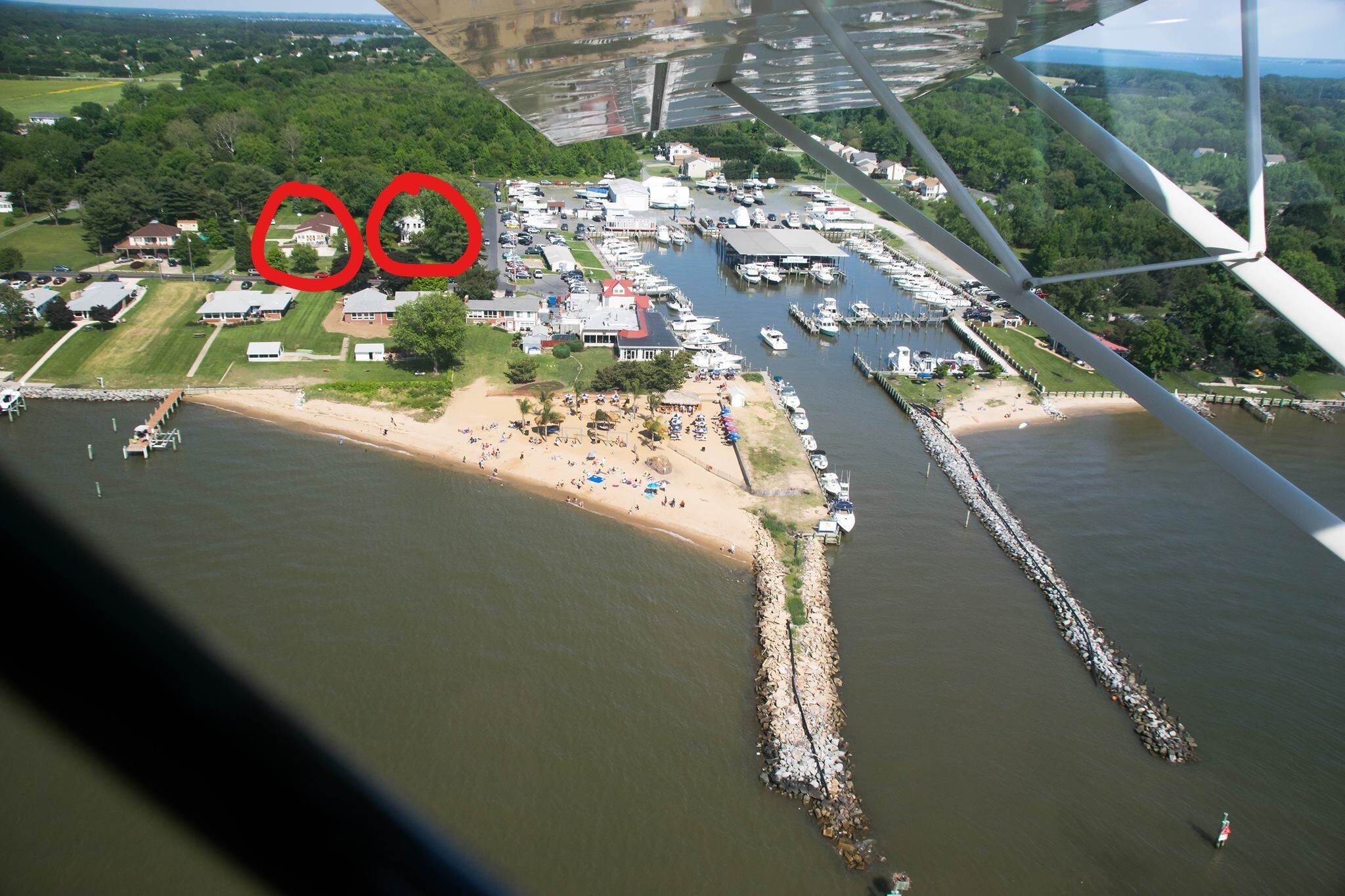Vue aérienne d’une marina avec des bateaux amarrés, une plage de sable et un pont en arrière-plan.