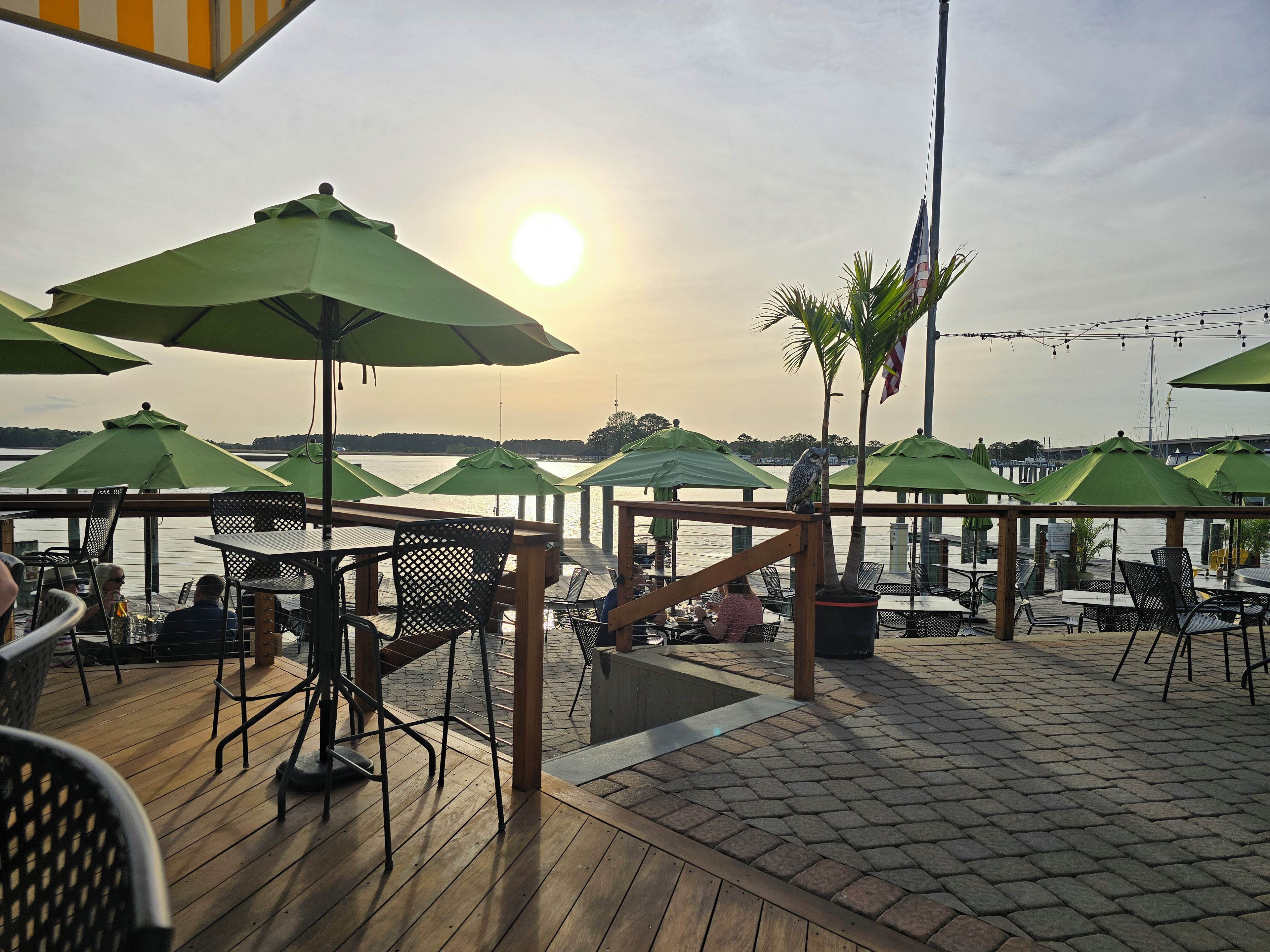 An outdoor seating area with tables and chairs, umbrellas, and a view of the water.