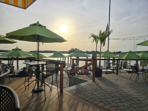 An outdoor seating area with tables and chairs, umbrellas, and a view of the water. - Waterview Home! Beach Volleyball! Near Wedding Venues! Walk to Bar & Restaurant! (Stevensville)