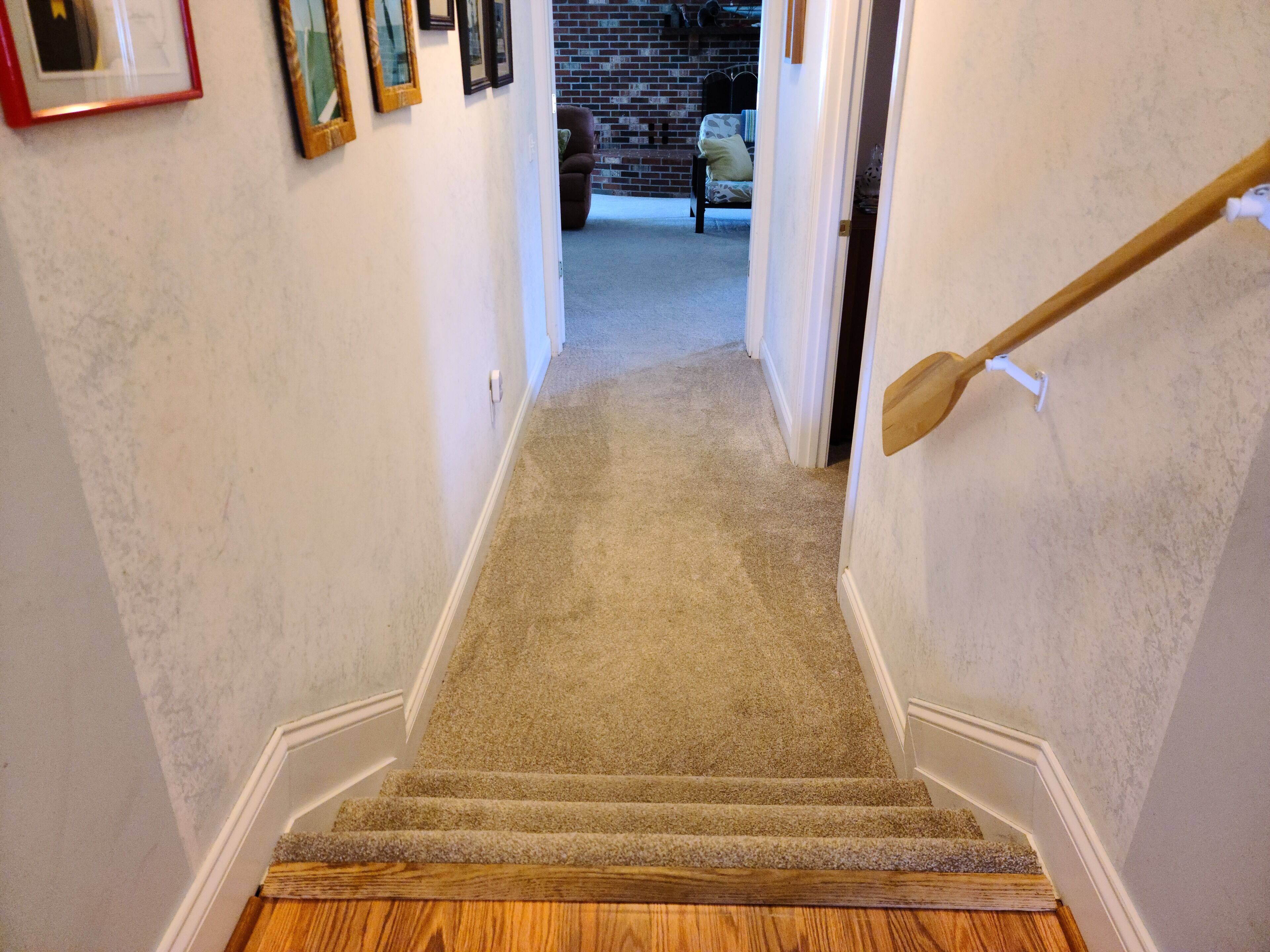 A carpeted staircase with wooden steps and a handrail, leading to a room with a brick wall and a chair.