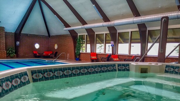 An indoor swimming pool with a tiled edge, red chairs, and a brick wall. - Remodeled Townhome in Excellent Location.Pool &Gym (Frisco)