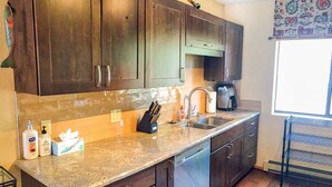 A kitchen with dark wooden cabinets, a granite countertop, a dishwasher, and a coffee maker. - Remodeled Townhome in Excellent Location.Pool &Gym (Frisco)