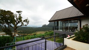 A balcony with a view of a lake and mountains, a building with large windows, and a tennis court. - Mount Lake Inn (Nuwara Eliya)