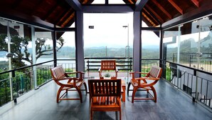 A balcony with a wooden table and chairs, offering a view of a mountainous landscape. - Mount Lake Inn (Nuwara Eliya)
