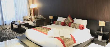 A hotel room with a large bed, a sitting area with a chair, a small table, and a lamp.