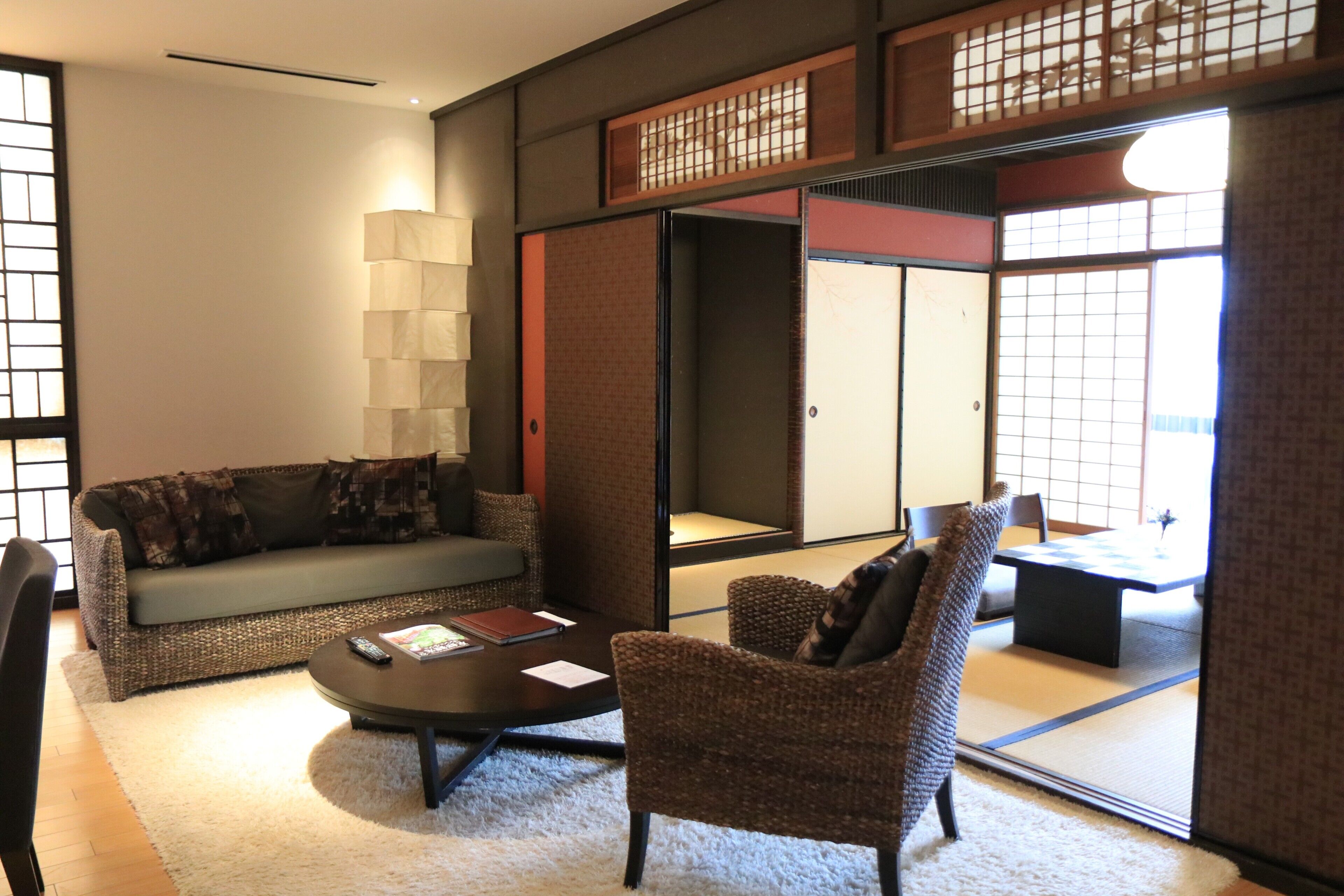 A traditional Japanese-style living room with tatami flooring, a low table, a sofa, and a chair.