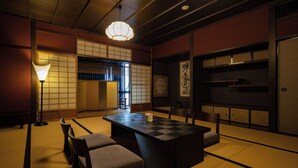 A traditional Japanese room with tatami flooring, a low table with cushions, a hanging light fixture, and sliding doors. - KIZASHI THE SUITE (Kyoto)