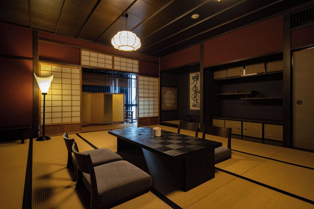 A traditional Japanese room with tatami flooring, a low table with cushions, a hanging light fixture, and sliding doors.