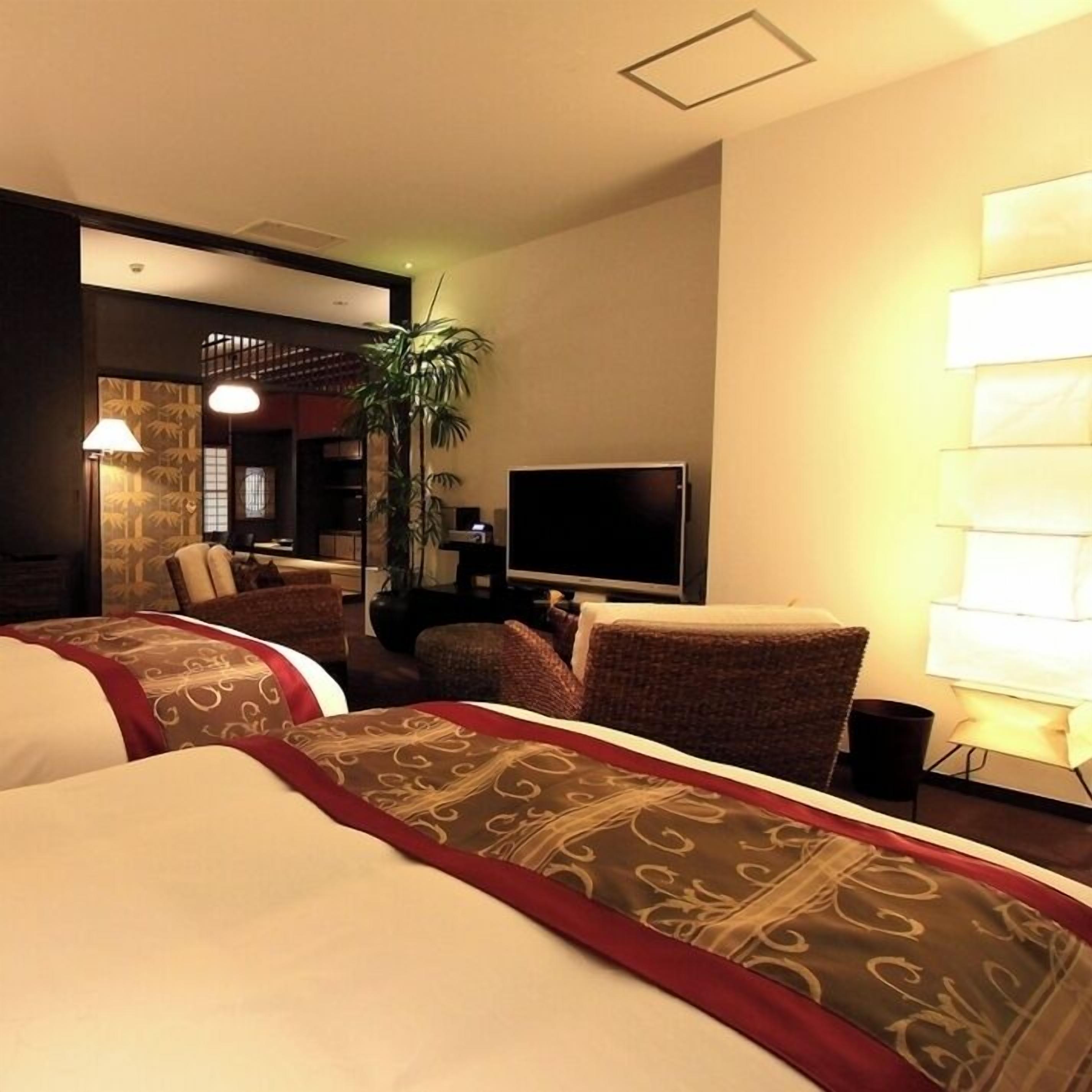 A hotel room with a bed, a TV, a chair, a lamp, and a plant.