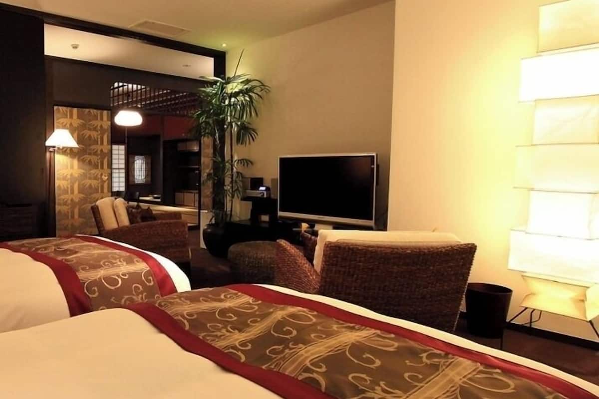 Une chambre d’hôtel avec un lit, une télévision, une chaise, une lampe et une plante.