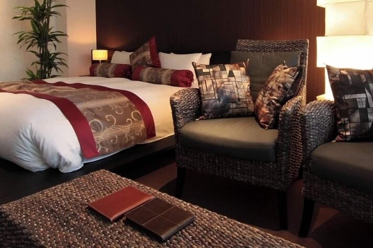 A hotel room with a bed, two armchairs, a side table, a lamp, and a potted plant.