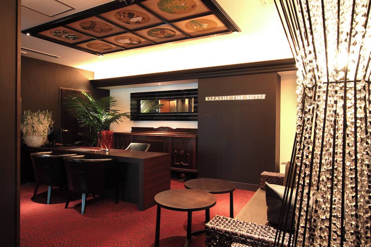 A hotel lobby with a reception desk, seating area, and a wall with a sign reading 'KIZASHI THE SUITE.'
