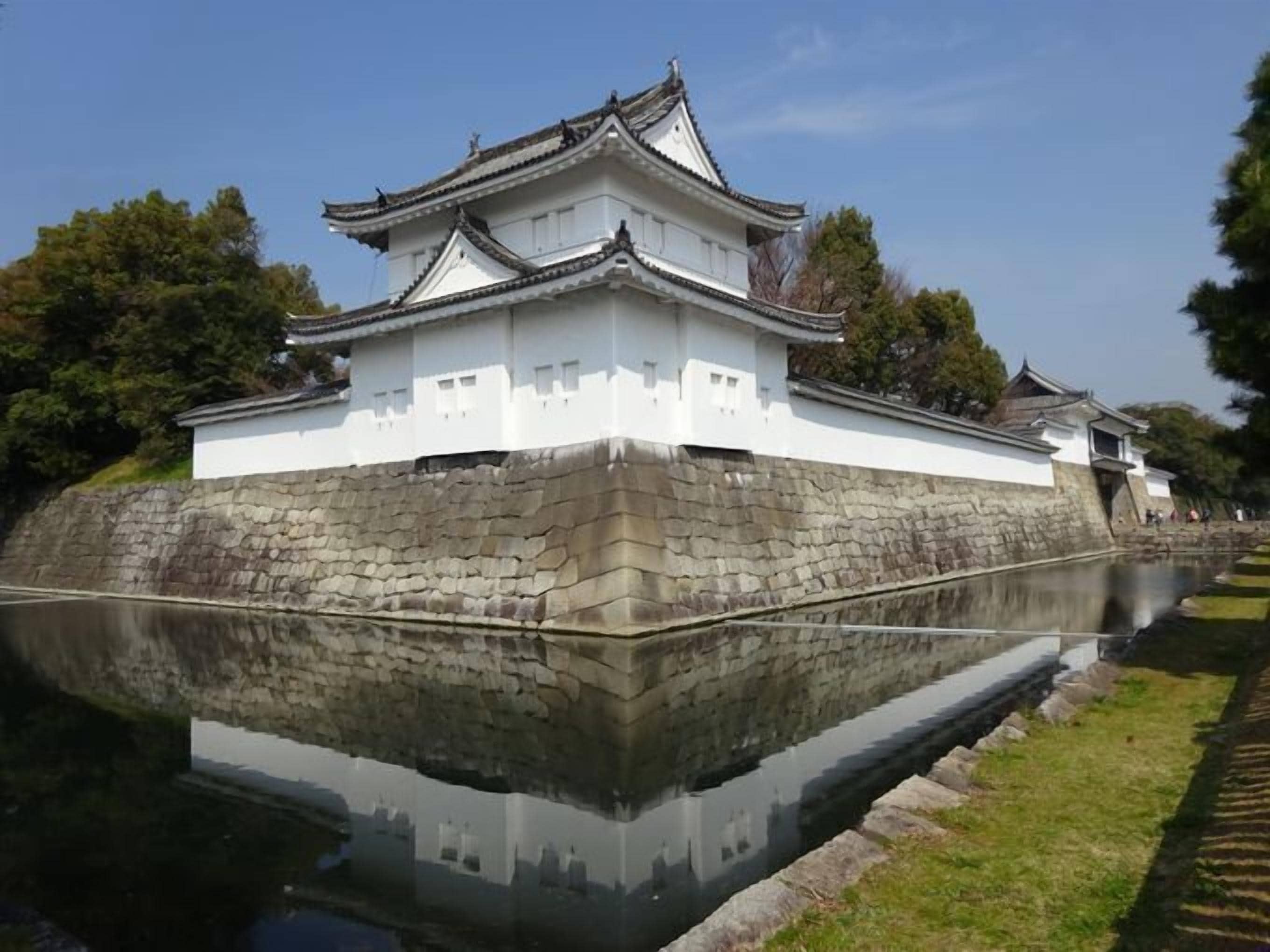 A traditional Japanese castle with a stone base and white walls, reflecting in a calm water body.