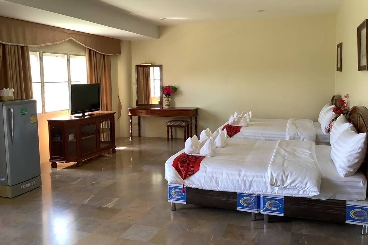 A hotel room with two beds, a desk, a television, and a refrigerator.