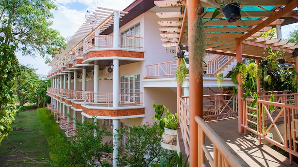 A multi-story hotel with balconies, outdoor seating, and potted plants. - Goldenland Resort (Chok Chai)