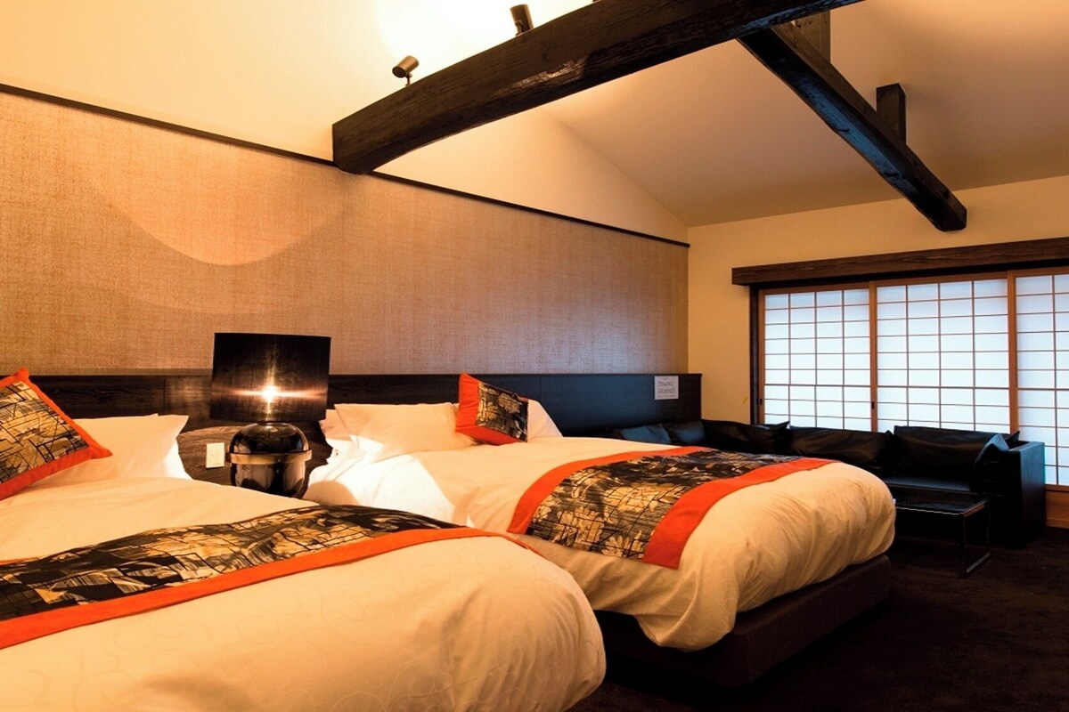 Ett hotellrum med två sängar, ett nattduksbord, en lampa, ett skrivbord och ett stort fönster med skjutpaneler i japansk stil.