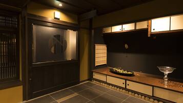 A room with a dark wooden door, a tiled floor, a wooden counter with a decorative bowl, and a small table with a glass object.
