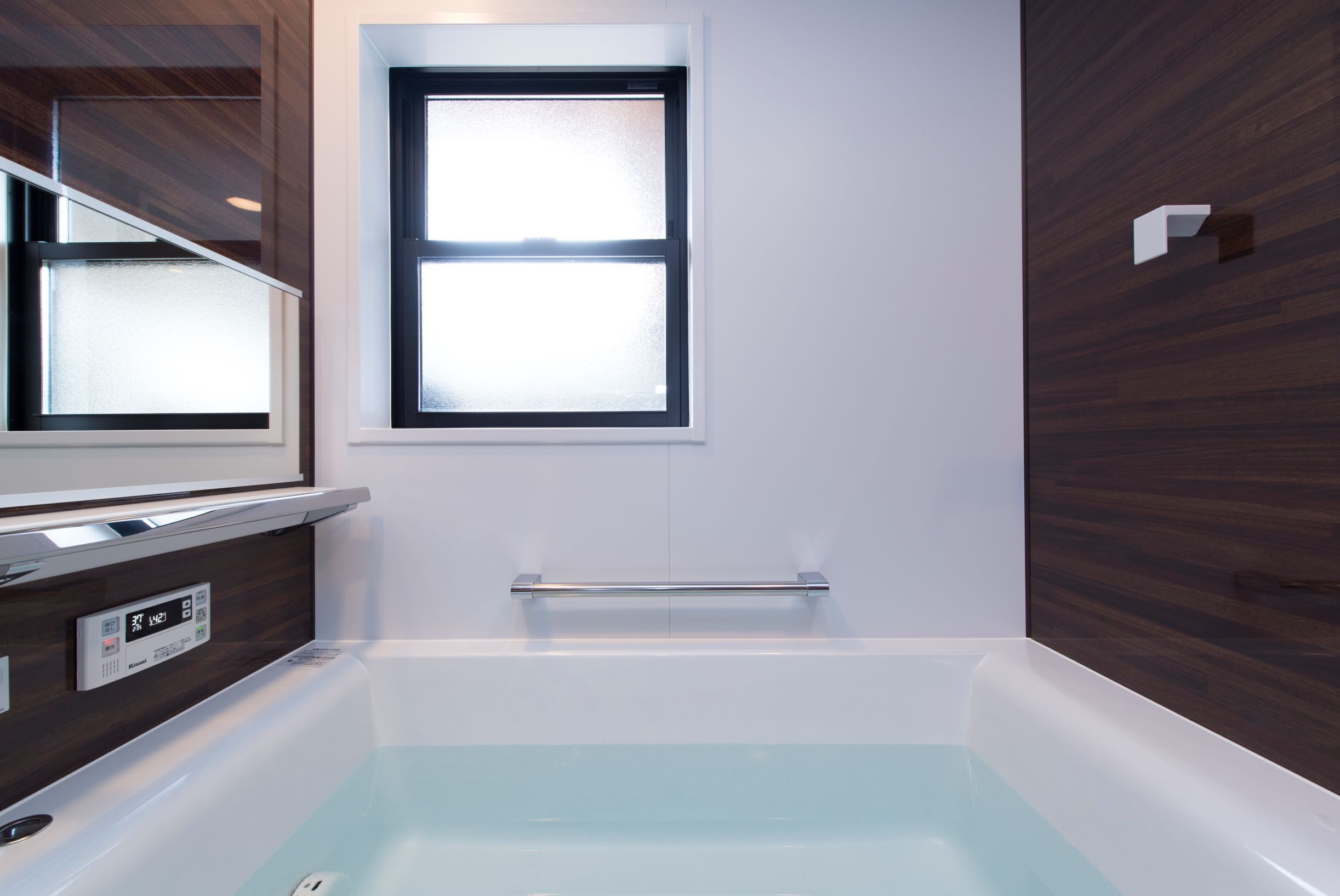 A modern bathroom with a bathtub, a window, and a control panel.