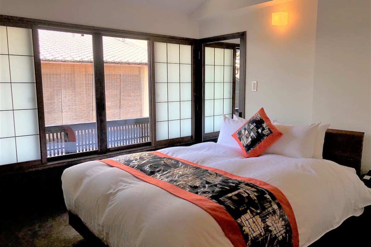 A hotel room with a large bed, a view through a sliding door, and a wall-mounted light.