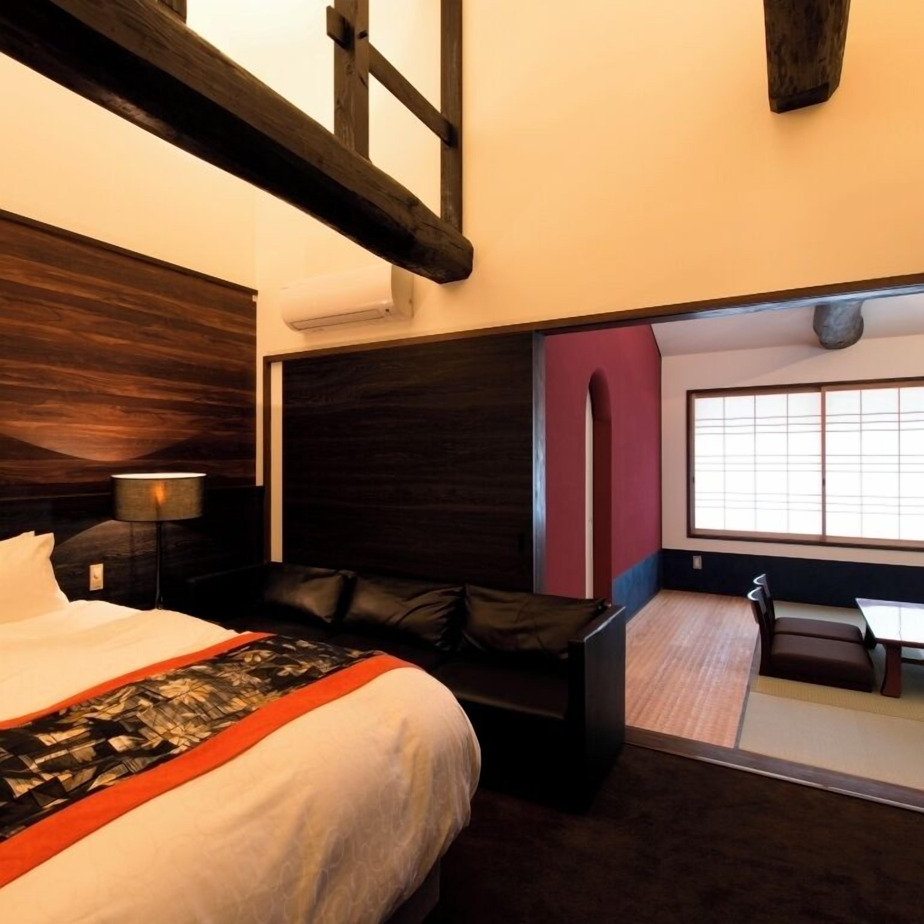 Quarto de hotel com uma cama grande, uma escrivaninha, uma cadeira, um sofá e vista para um quarto japonês tradicional.