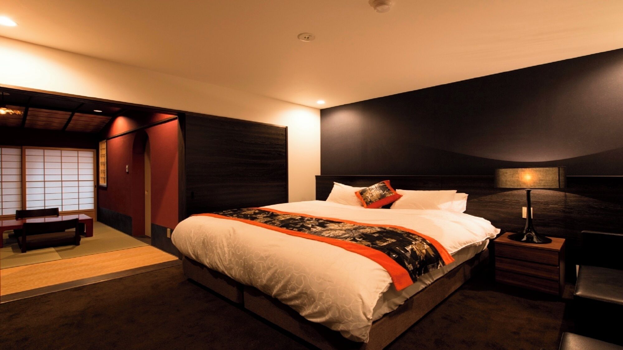 Quarto de hotel moderno com uma cama grande, mesa de cabeceira e uma porta japonesa tradicional.