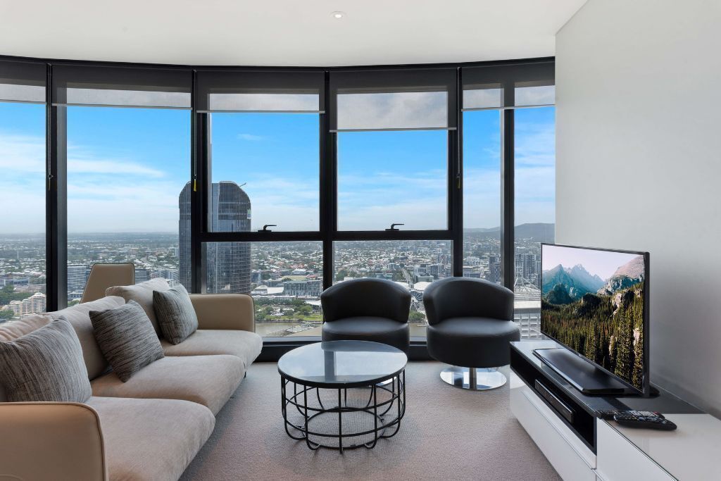 A modern living room with a large window, a sofa, two armchairs, a coffee table, and a flat-screen TV.