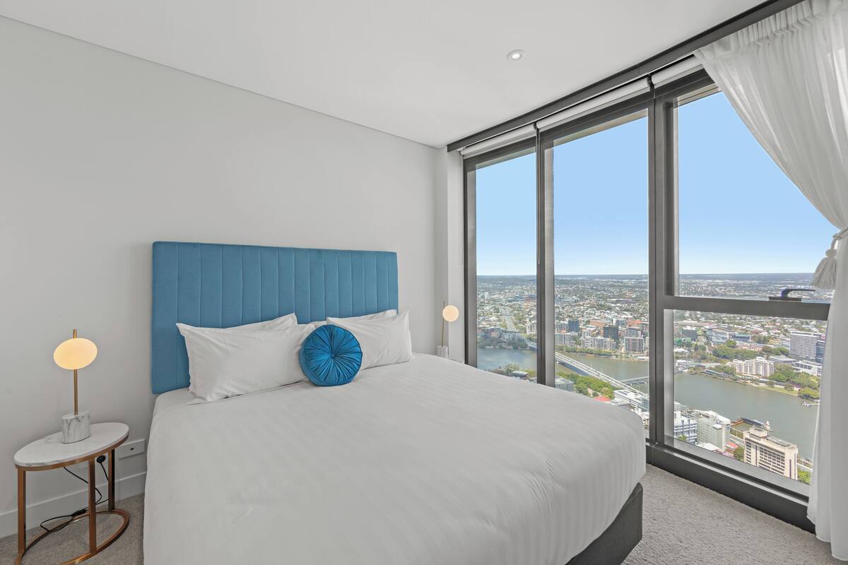 A modern hotel room with a large bed, a view of a cityscape, and a city river.