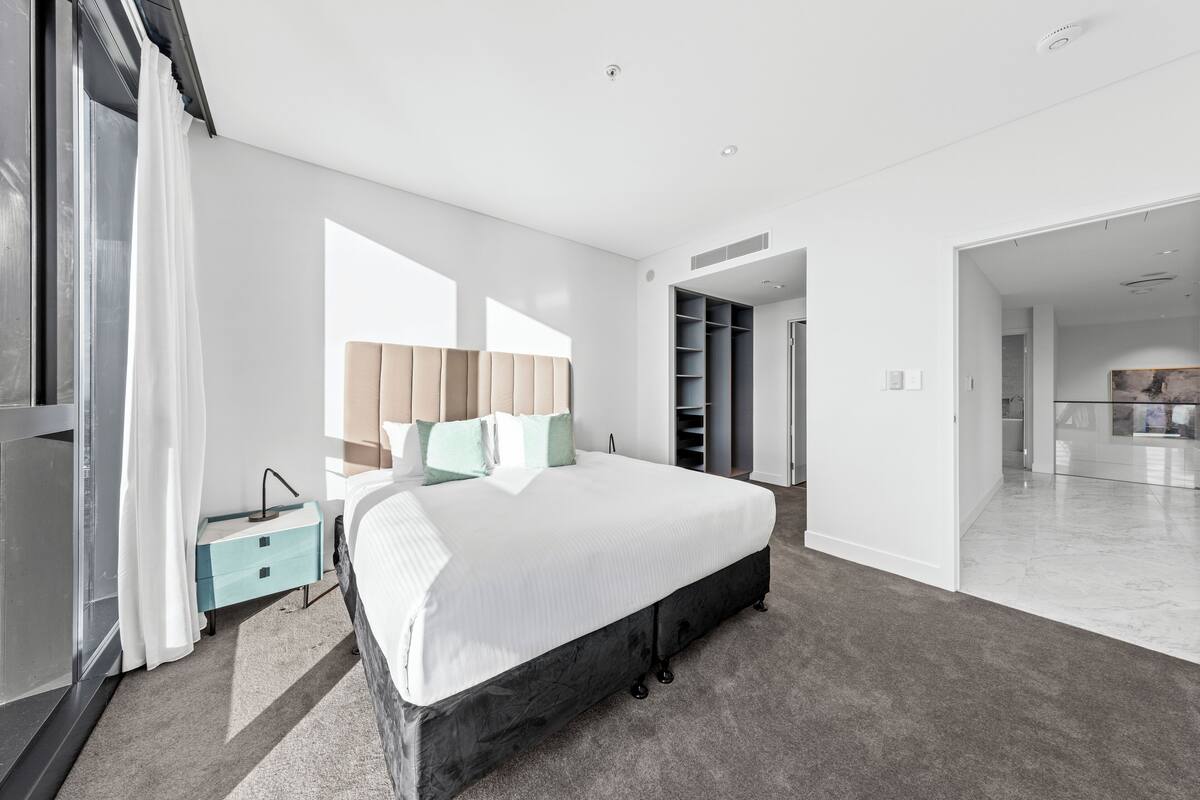A modern bedroom with a large bed, a nightstand, a wardrobe, and a bathroom visible through an open door.