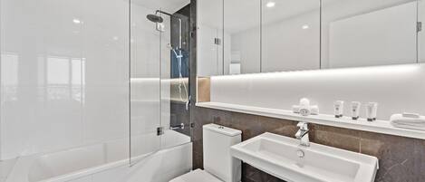 A modern bathroom with a glass-enclosed shower, a white toilet, a sink, and a mirror above the sink.