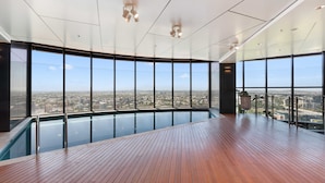 A spacious indoor pool area with a panoramic city view, modern lighting fixtures, and a wooden deck. - CLLIX Brisbane Skytower Apartments (Brisbane)