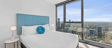 A modern hotel room with a large bed, a city view, and a small side table with a lamp.