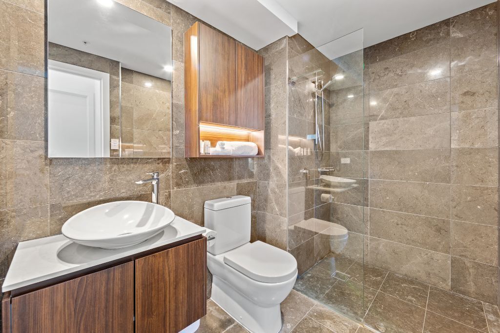 A modern bathroom with a large mirror, a wooden vanity, a toilet, and a glass-enclosed shower area.