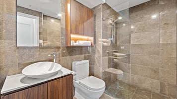 A modern bathroom with a large mirror, a wooden vanity, a toilet, and a glass-enclosed shower area.