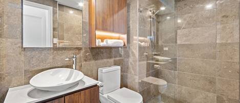 Une salle de bain moderne avec un grand miroir, un meuble-lavabo en bois, des toilettes et une douche séparée par une paroi de verre.