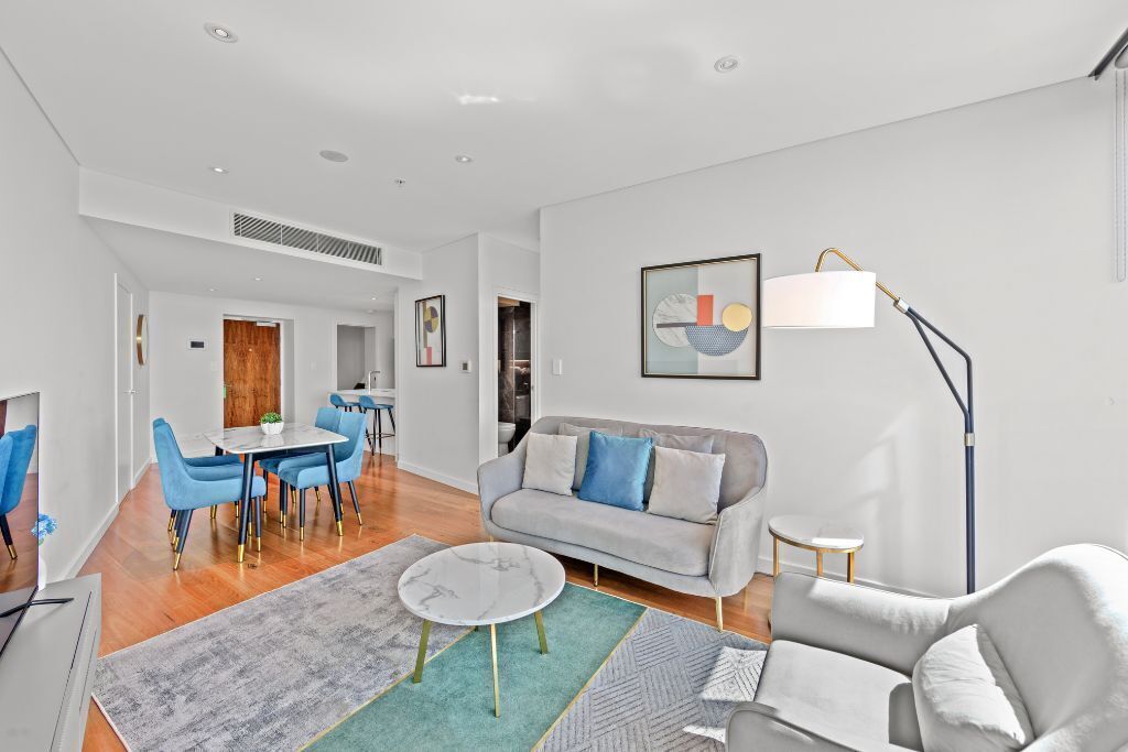 A modern living room with a grey sofa, blue chairs, a dining area with a table and chairs, and a floor lamp.