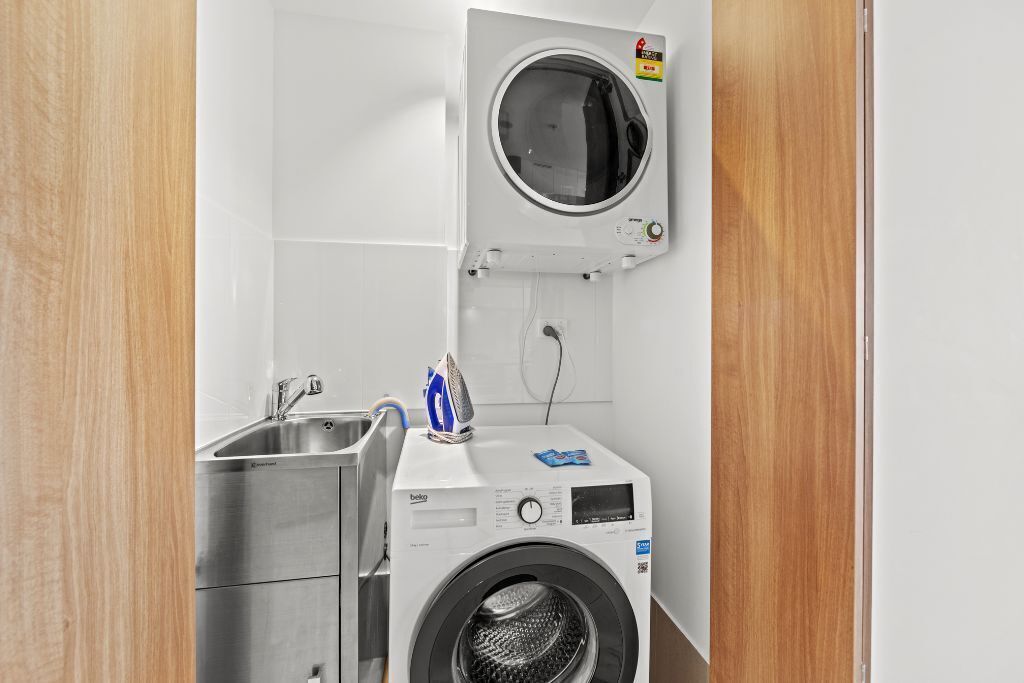 Un espace buanderie compact comprenant un lave-linge, un sèche-linge, un évier et une petite planche à repasser.