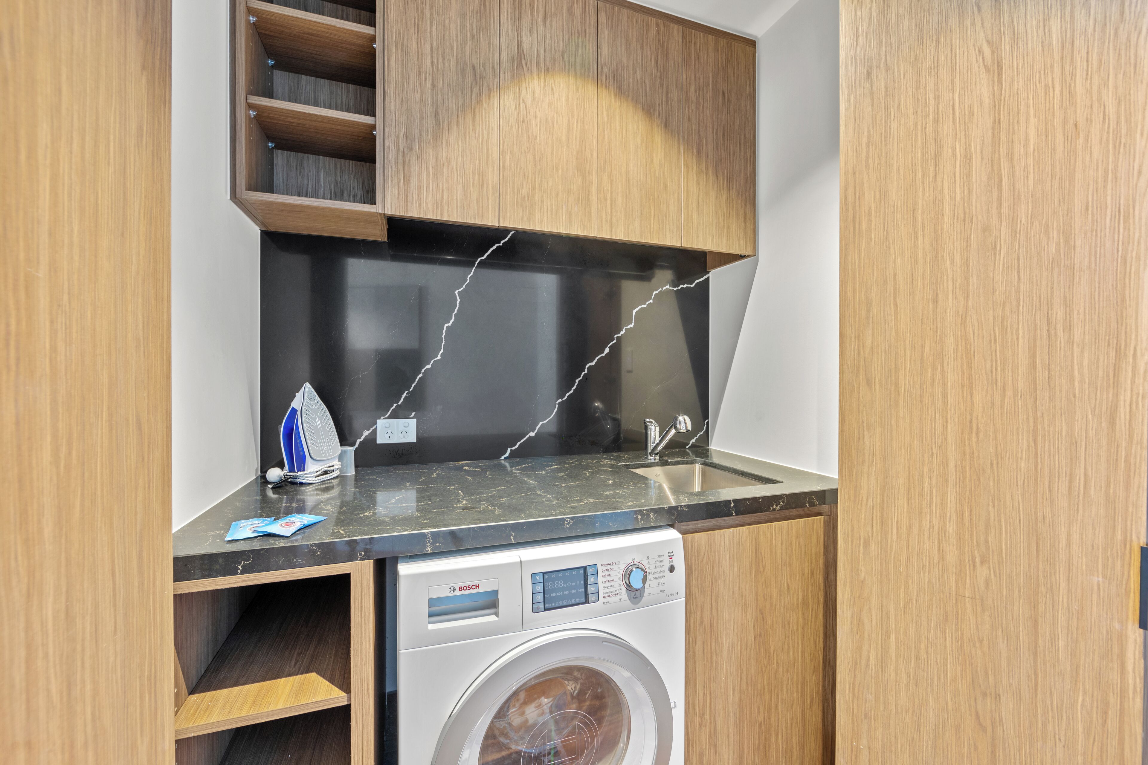 Una cocina compacta con lavadora Bosch, una encimera negra y armarios de madera.