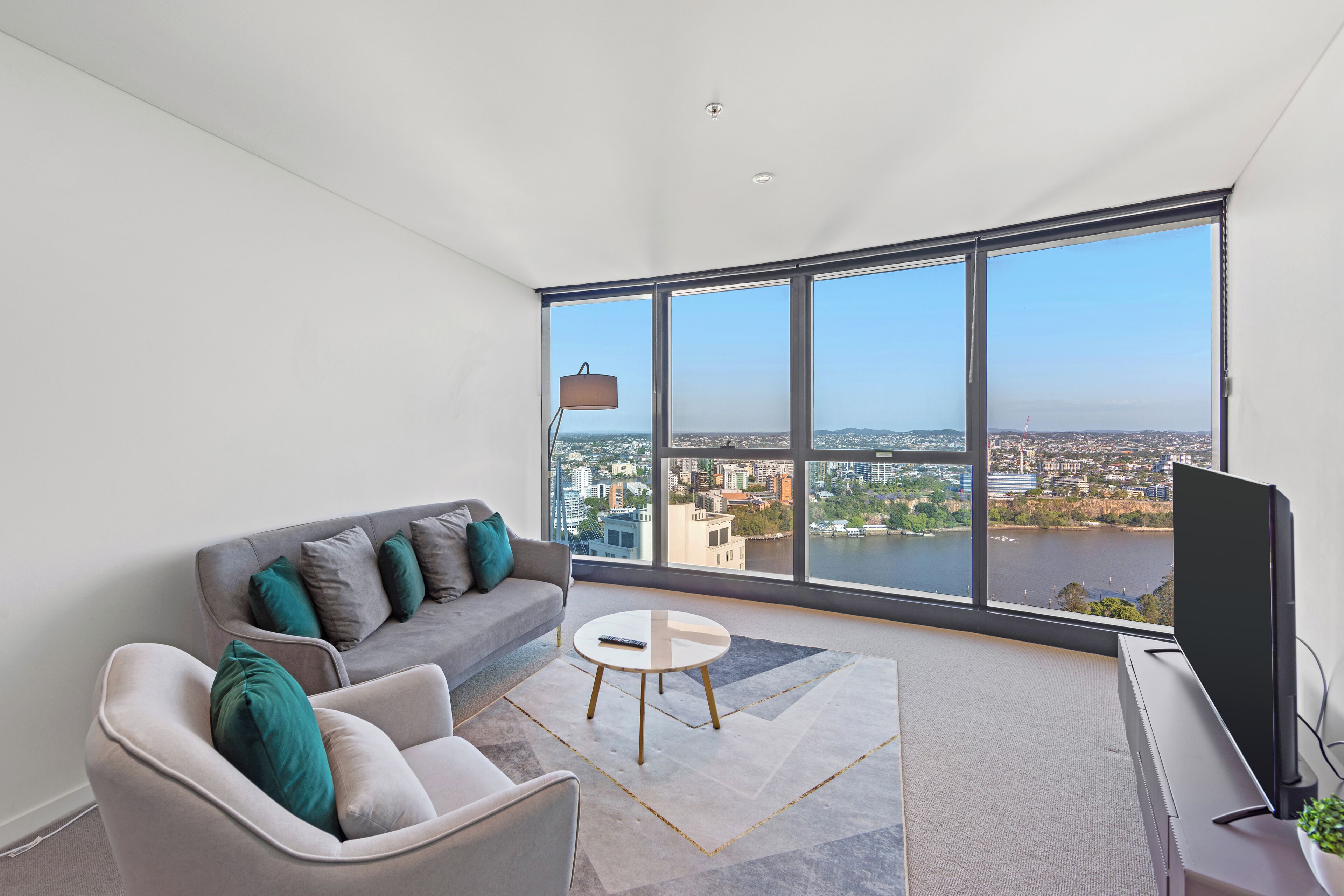 A modern living room with a sofa, armchair, and coffee table, a flat-screen TV, and a large window offering a city view.