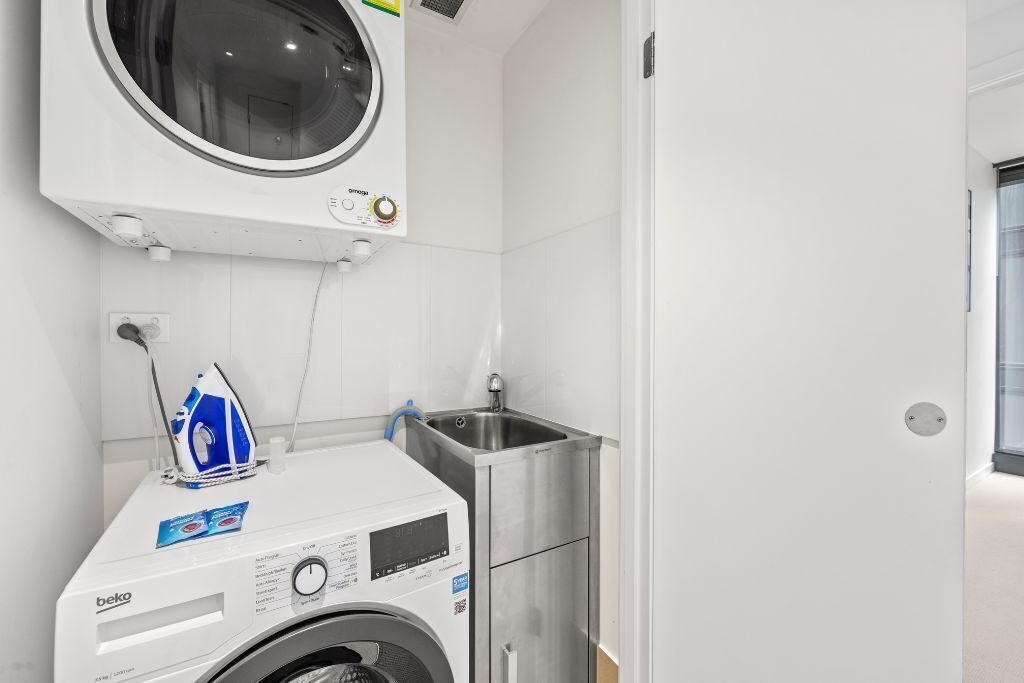 Un espace buanderie compact comprenant un lave-linge à chargement frontal, un sèche-linge encastré et un petit évier.