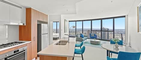 A modern kitchen with a central island, stainless steel appliances, and large windows offering a city view.