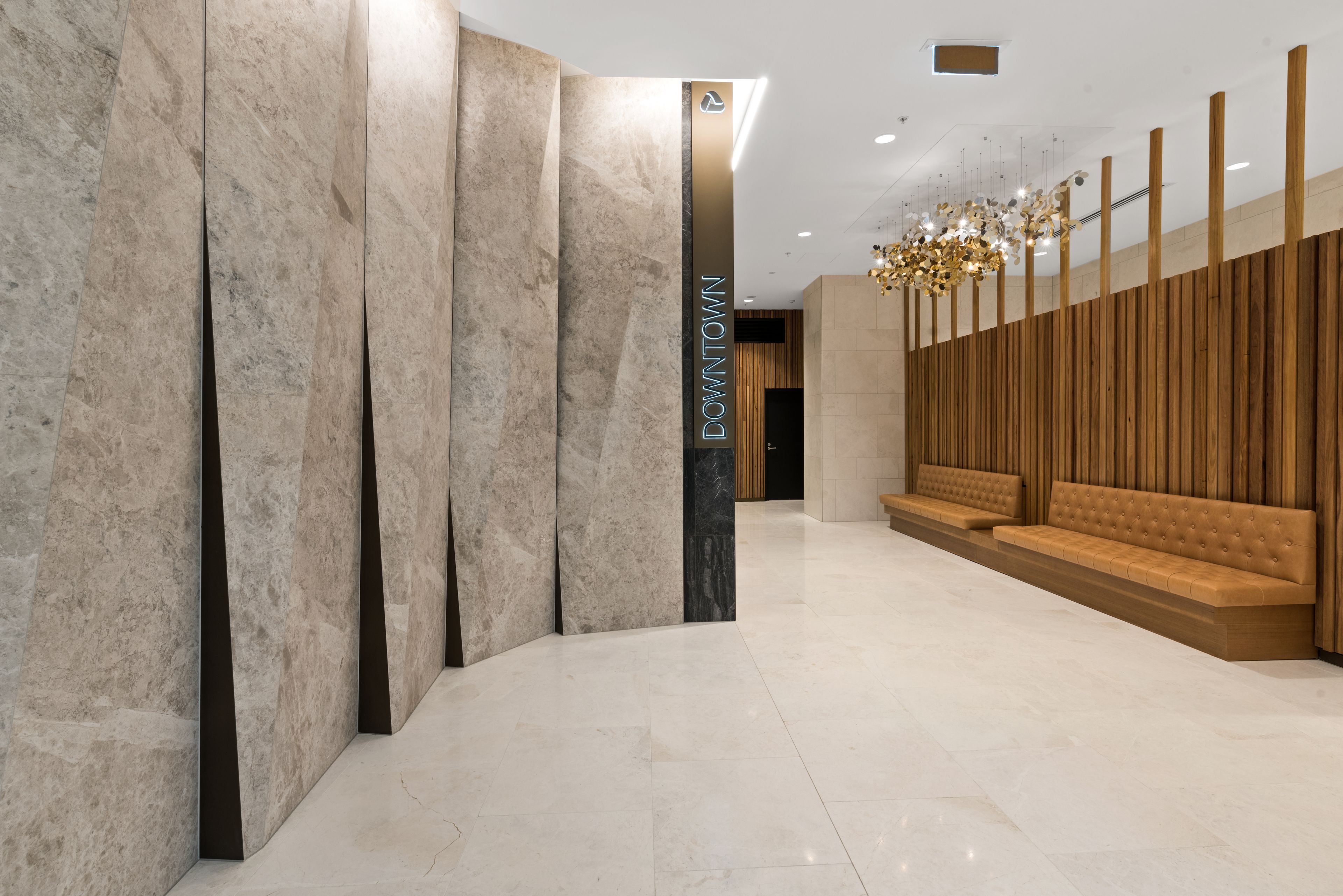 Un hall d’entrée moderne aux murs de marbre, avec une colonne centrale portant l’inscription « CENTRE-VILLE », et un espace détente agrémenté de panneaux en bois et d’un lustre.
