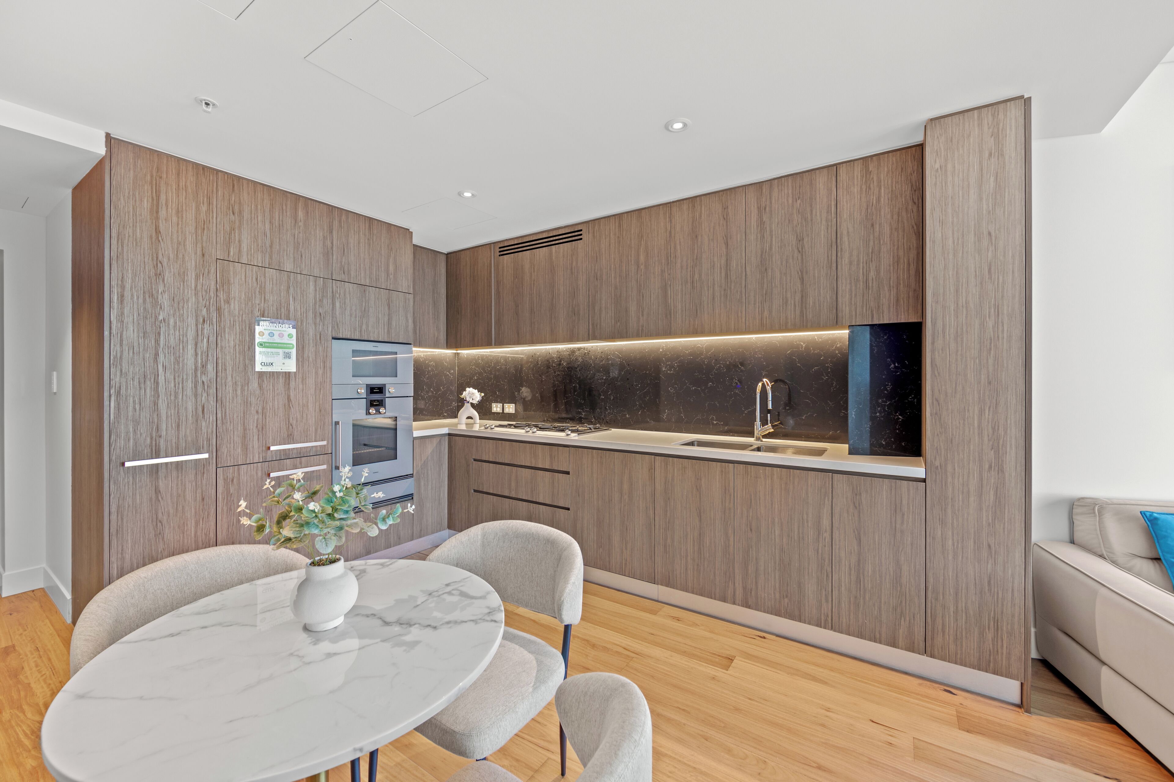 A modern kitchen with wood paneling, a built-in oven, and a marble countertop.