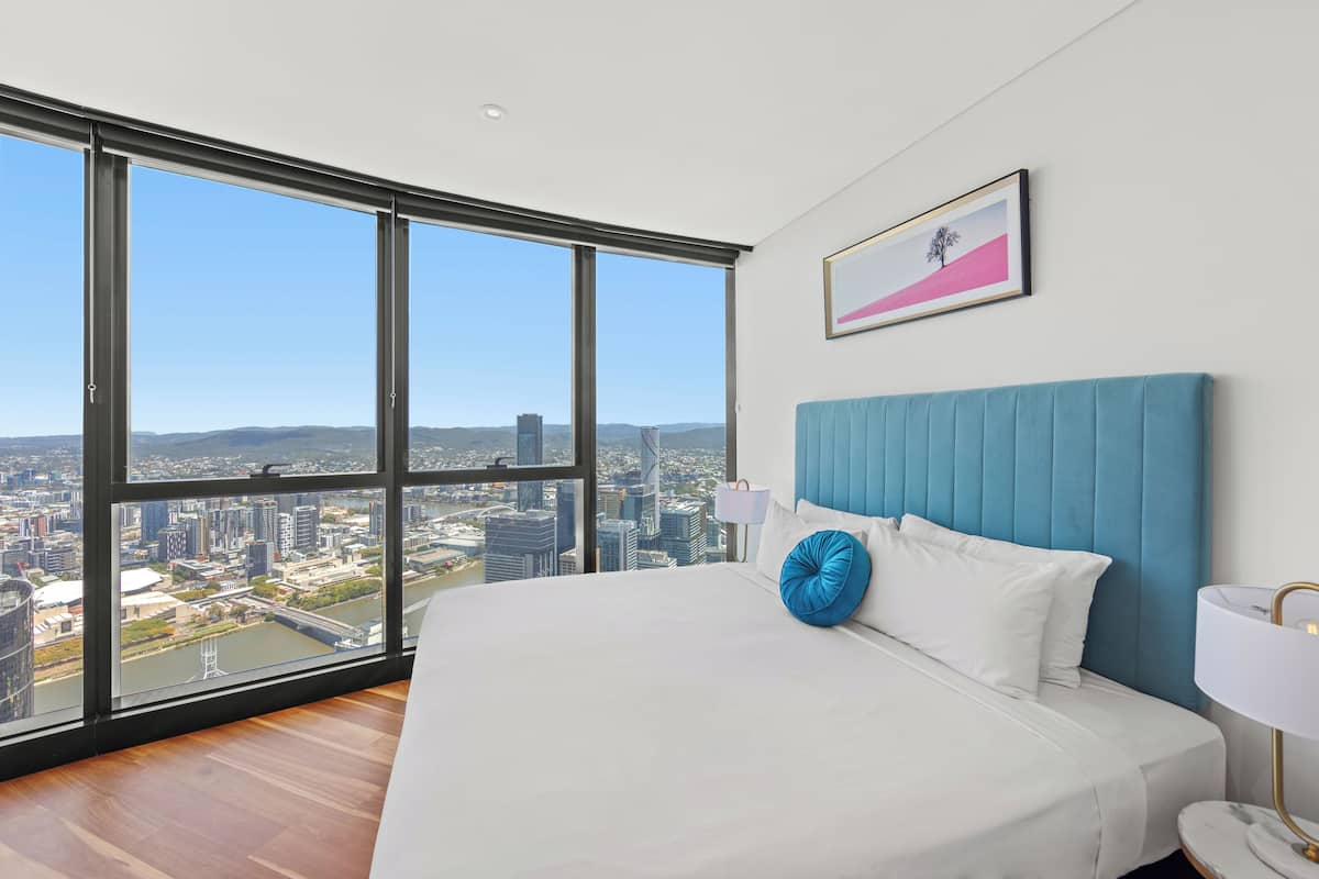 A modern hotel room with a large bed, a view of a cityscape, and a framed picture on the wall.