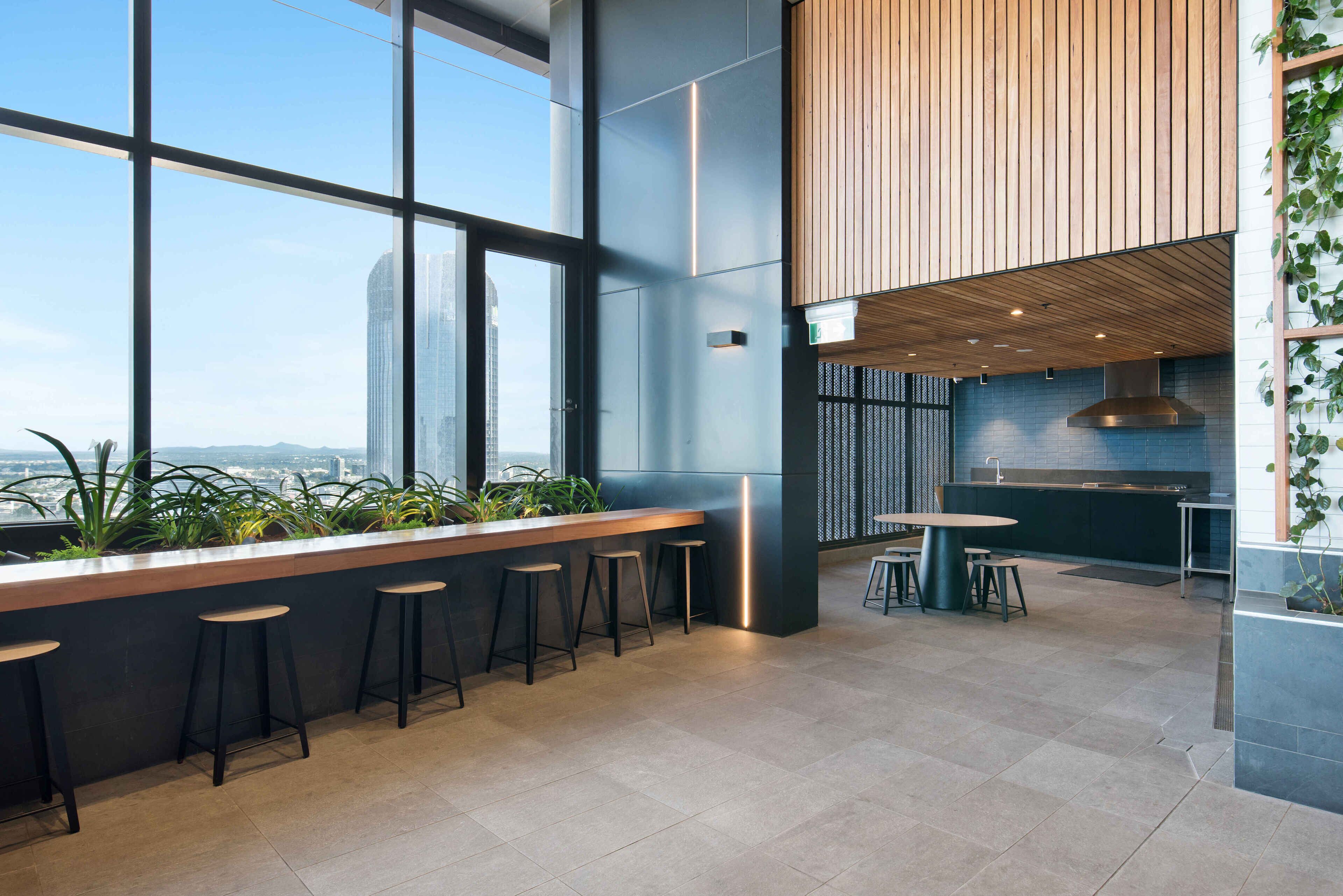 Zona de bar moderna con una barra alargada, varios taburetes y vistas de la ciudad a través de amplios ventanales.