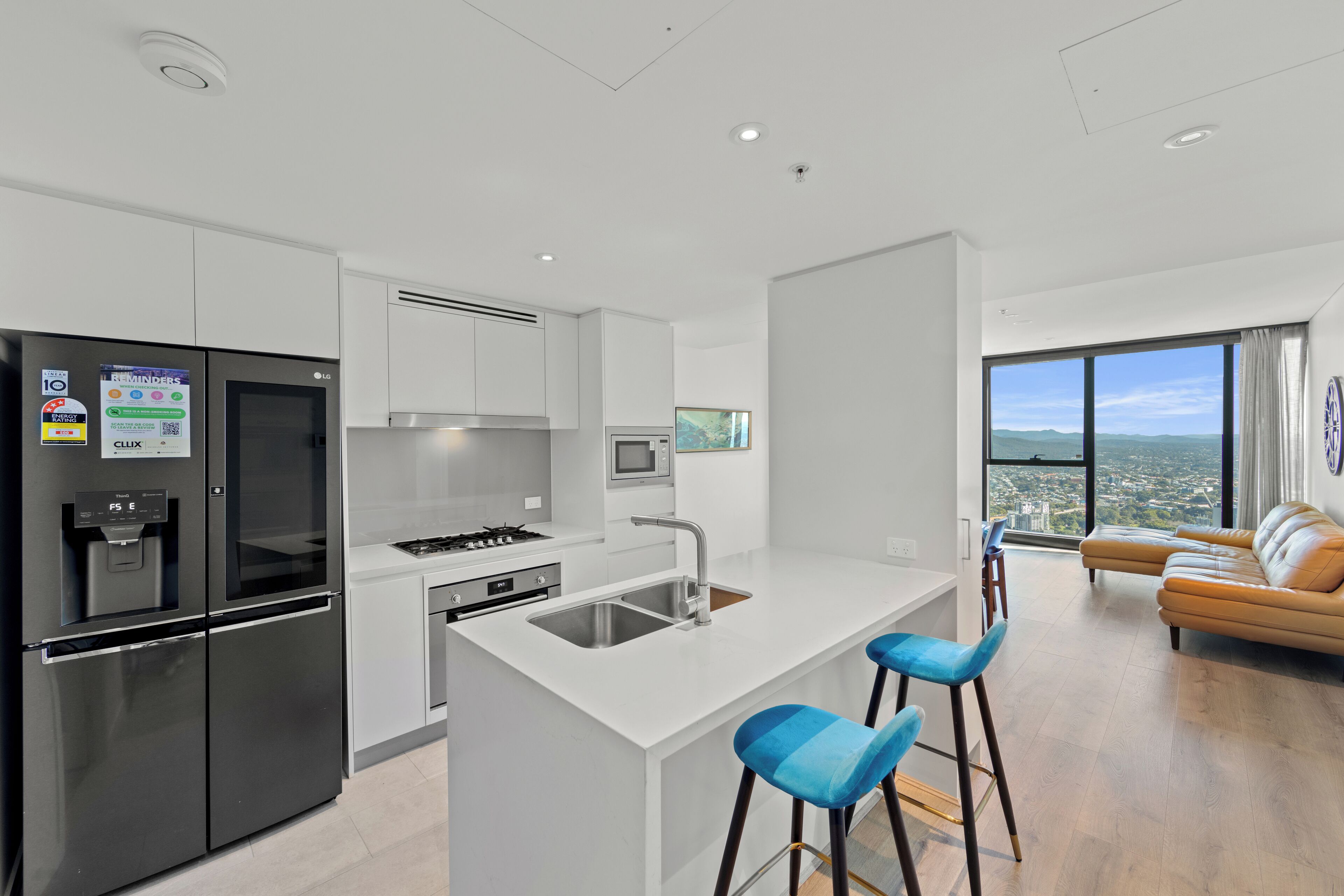 A modern kitchen with a central island, stainless steel appliances, and a view of the city through large windows.