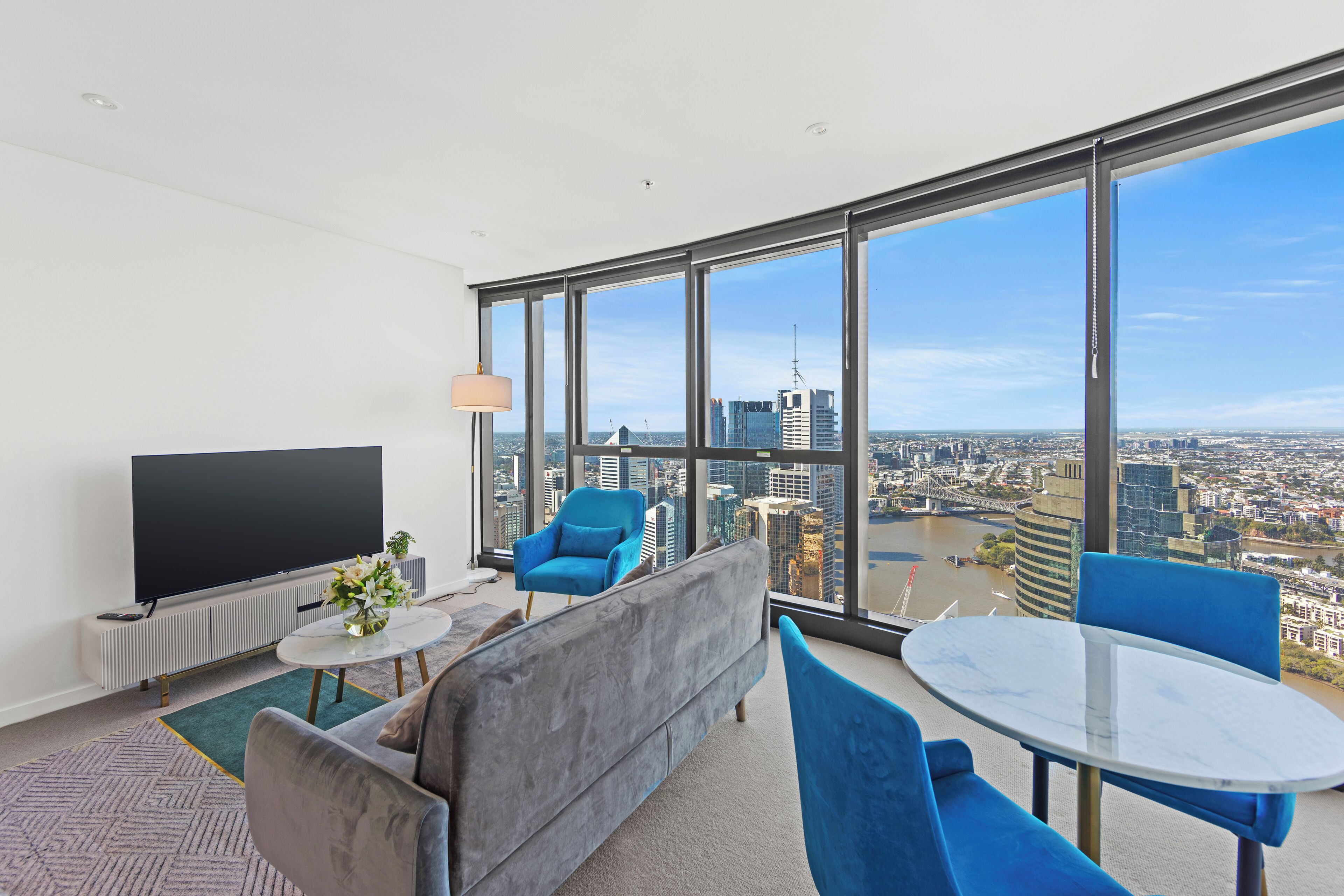 A modern living room with a large TV, comfortable seating, and a view of a cityscape through large windows.