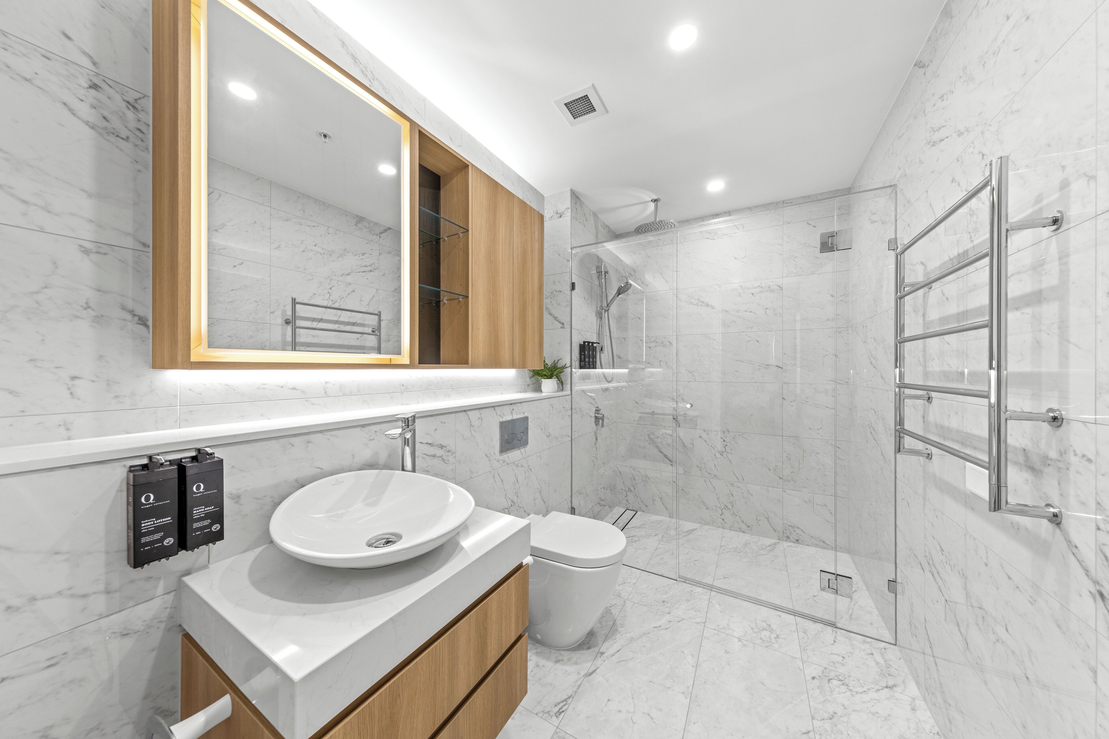 A modern bathroom with a marble sink, a large mirror, and a glass-enclosed shower.