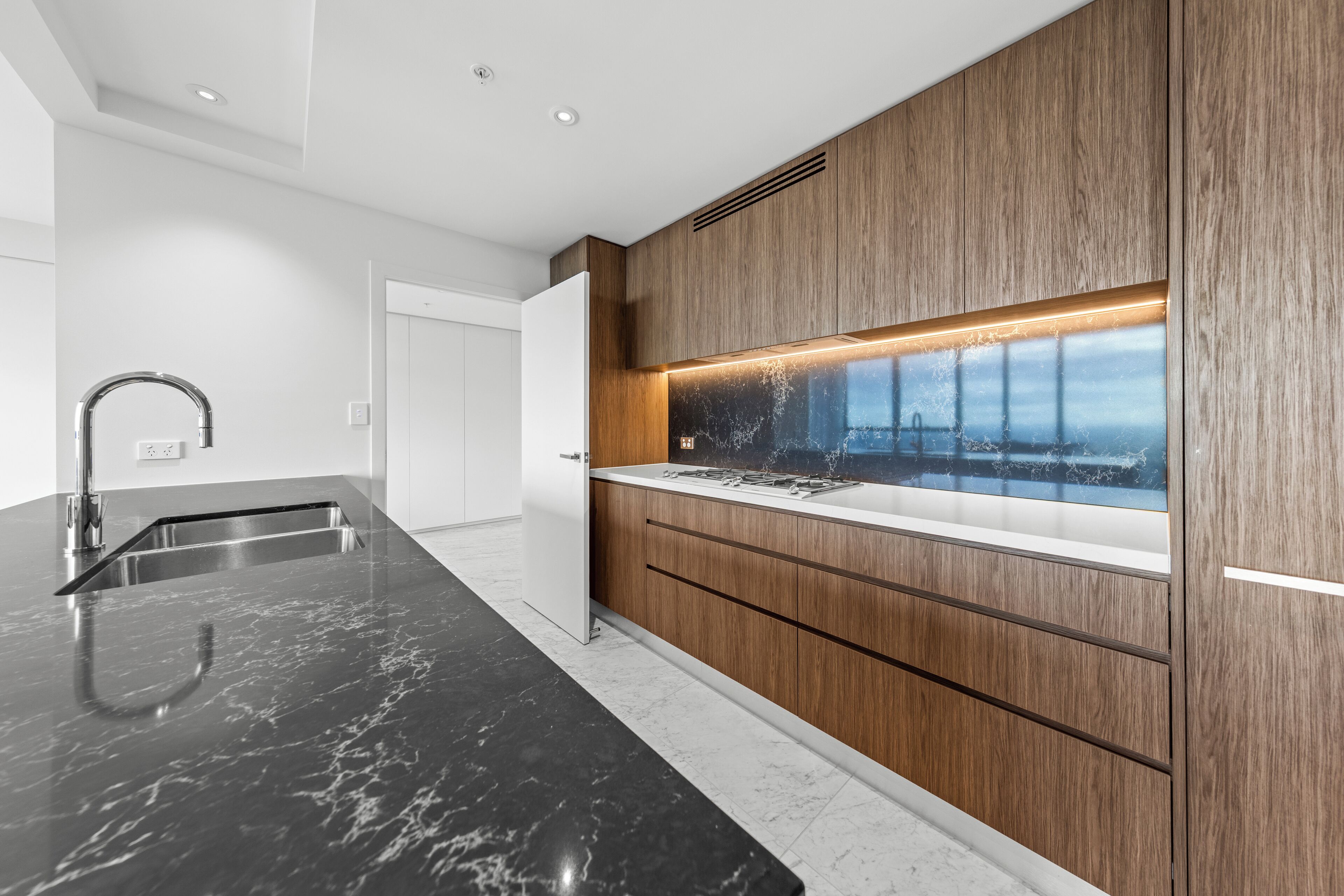 Een moderne keuken met een donker marmeren aanrechtblad, houten keukenkastjes en een inbouwfornuis.