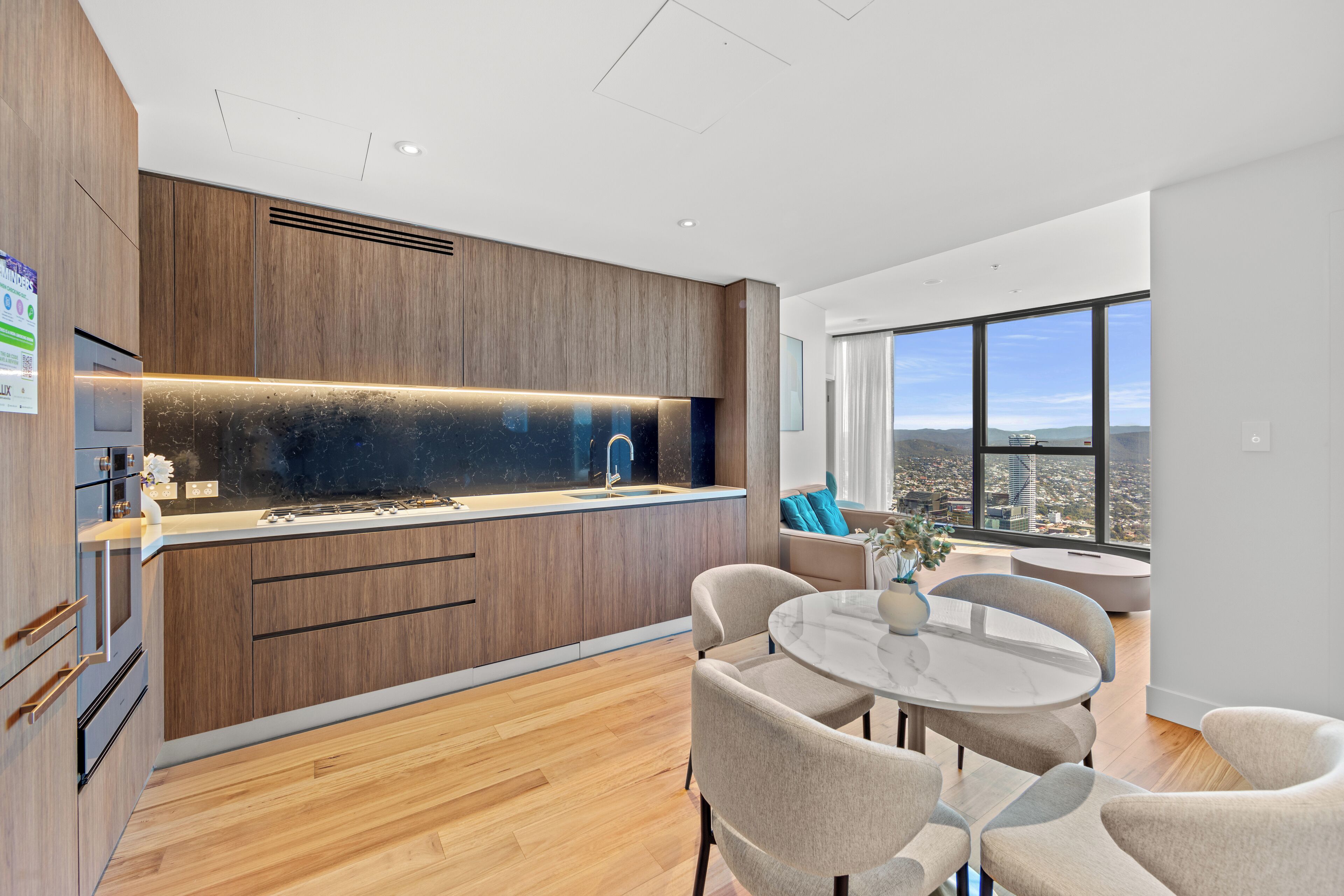 A modern kitchen with wooden cabinets, a marble countertop, and a city view through large windows.