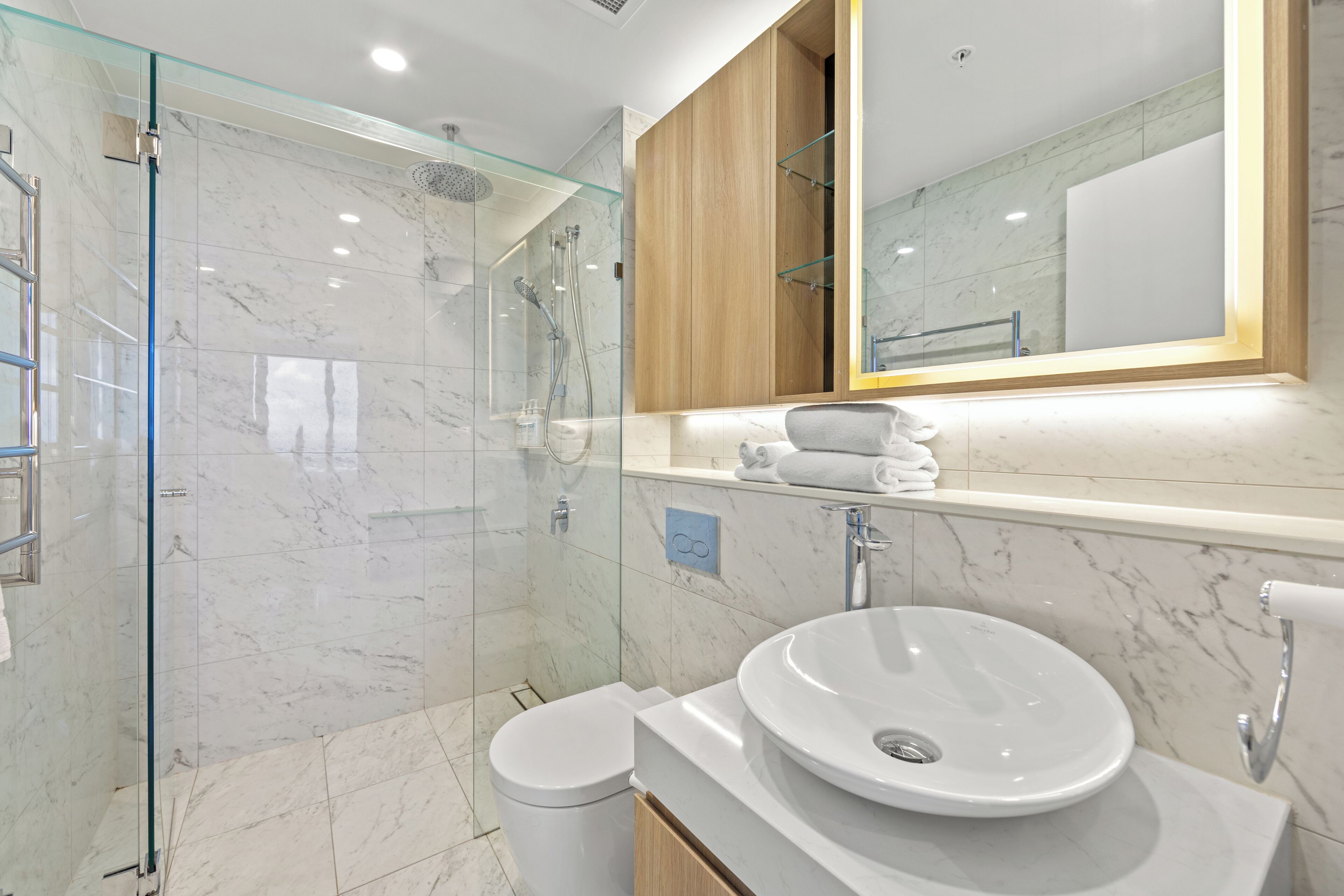 A modern bathroom with a glass-enclosed shower, a white sink, and a wooden vanity.
